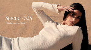 Malli makaa uurretussa, luonnonvalkoisessa "Almond White Pointelle Beach Dress" -mekossa hiekkarannalla lämpimässä ja aurinkoisessa ympäristössä. Bannerissa on myös teksti "Serene - S25" ja "Effortless essentials".